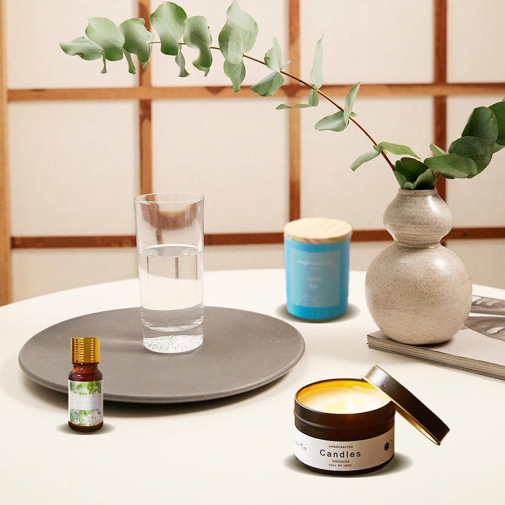 Scented candle in a tin with lid open, next to a glass of water, essential oil bottle, and decorative vase with eucalyptus.