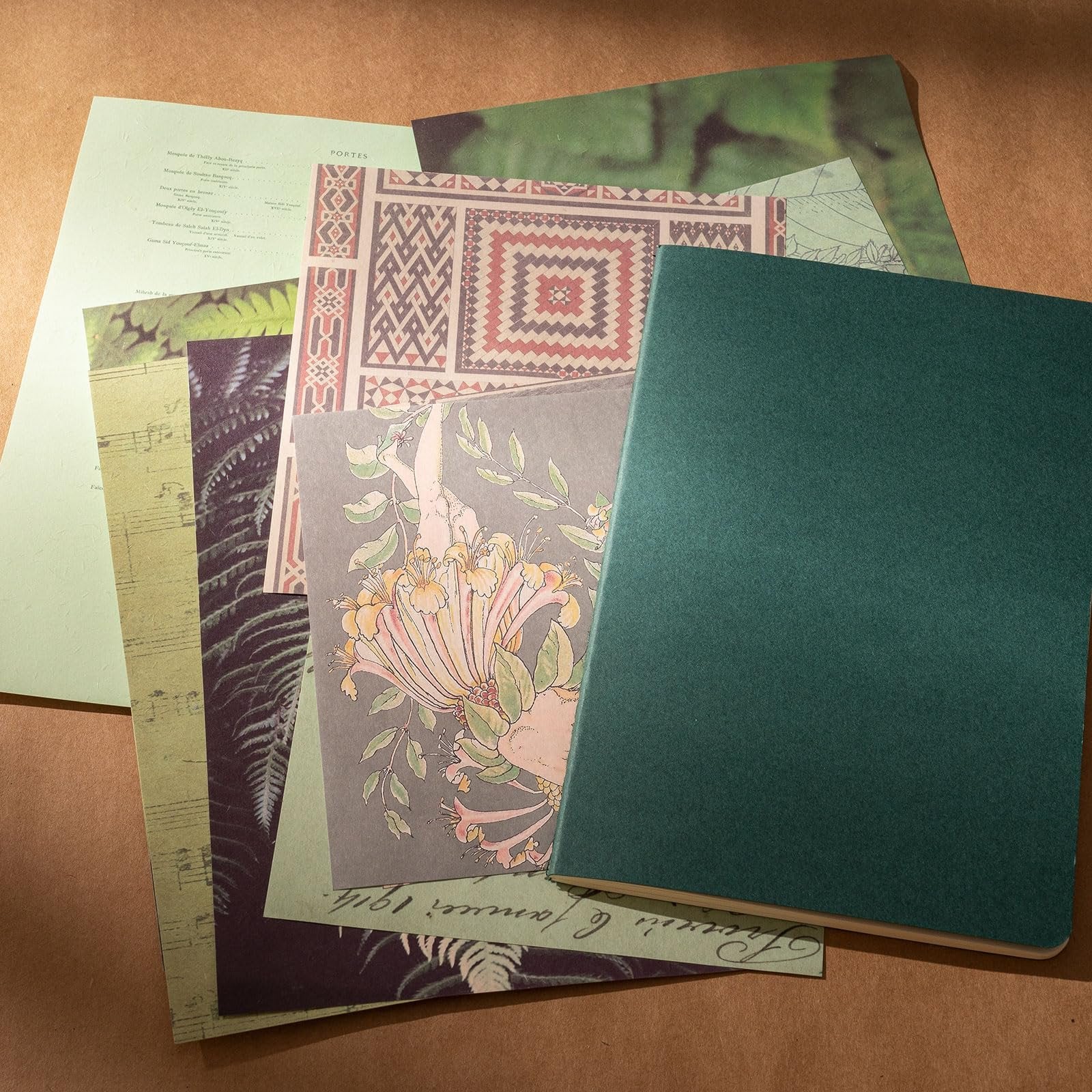 A stack of decorative papers and a dark green journal, featuring floral and geometric patterns, and sheet music.