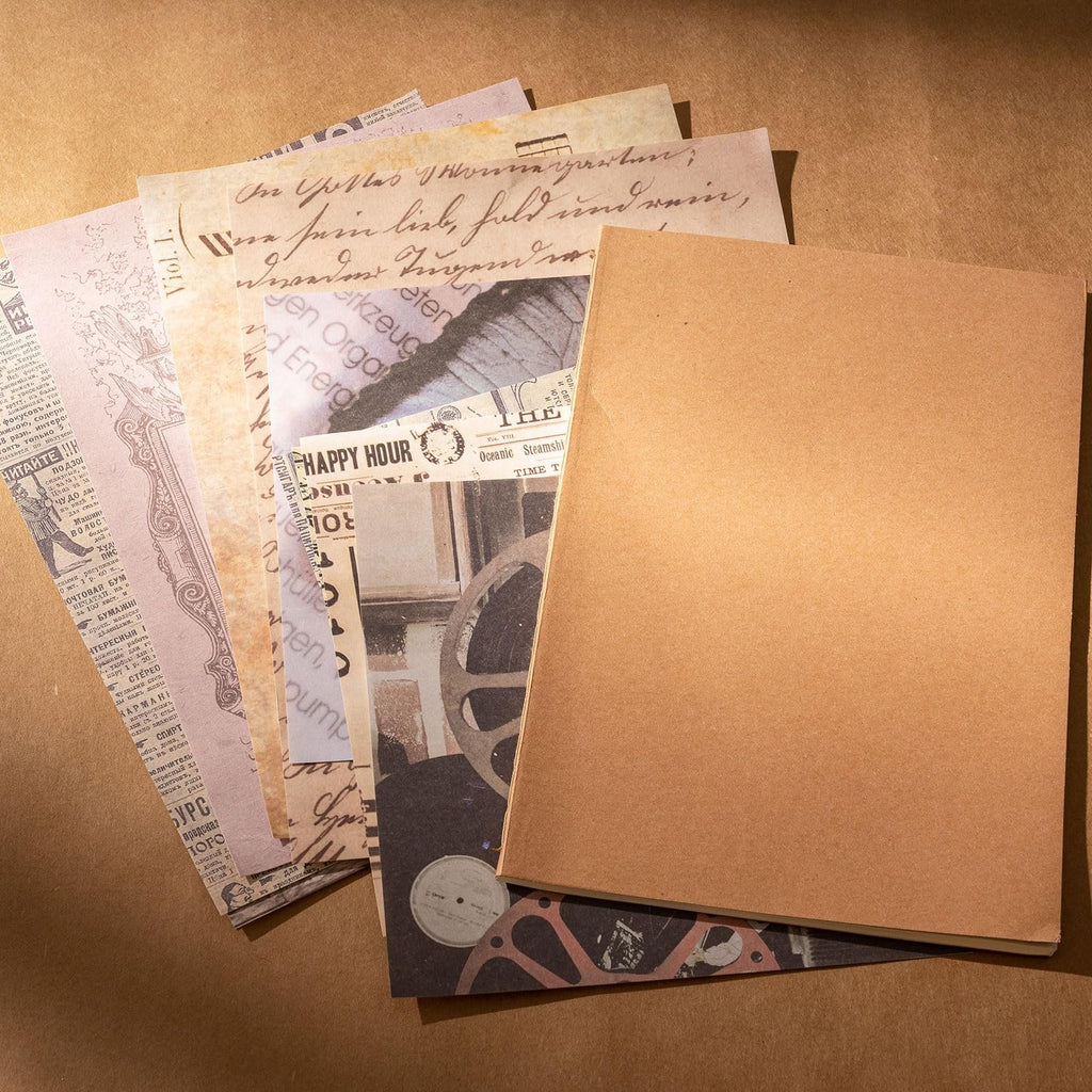 A stack of vintage-style papers with text and images, next to a plain brown notebook. Papers include handwritten script, newspaper clippings, and illustrations.