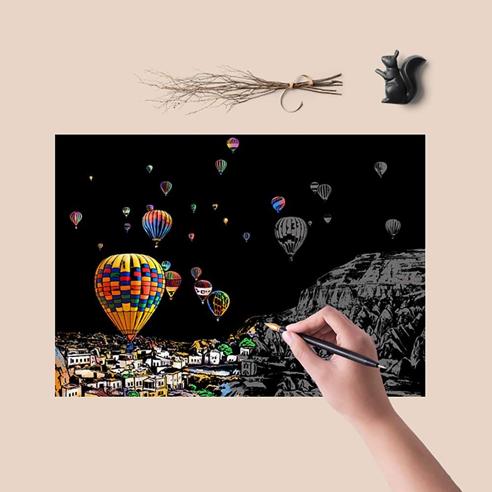 Scratch art card showing hot air balloons over a town and mountains, with a hand scratching the surface.