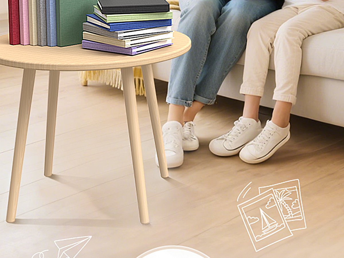 Two people sitting on a couch with a stack of books on a small wooden table, with sketched photos on the floor.