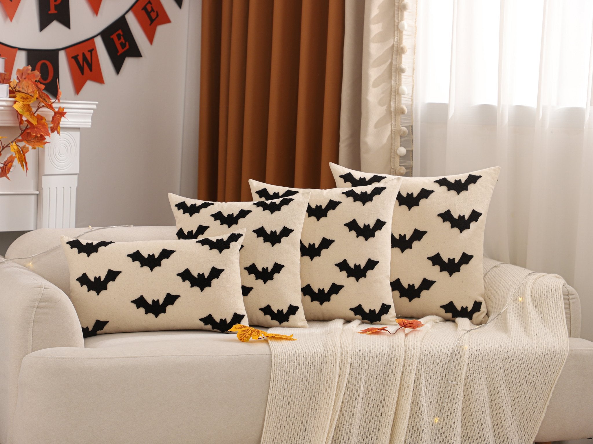 Four Halloween-themed throw pillow covers with black bat embroidery arranged on a sofa with a white throw blanket.
