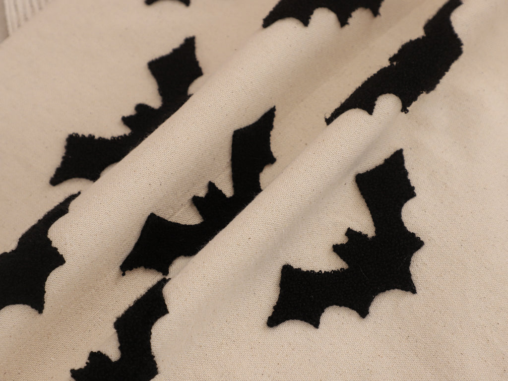 Close-up of a cream-colored fabric with black embroidered bat shapes, showing texture and detail.