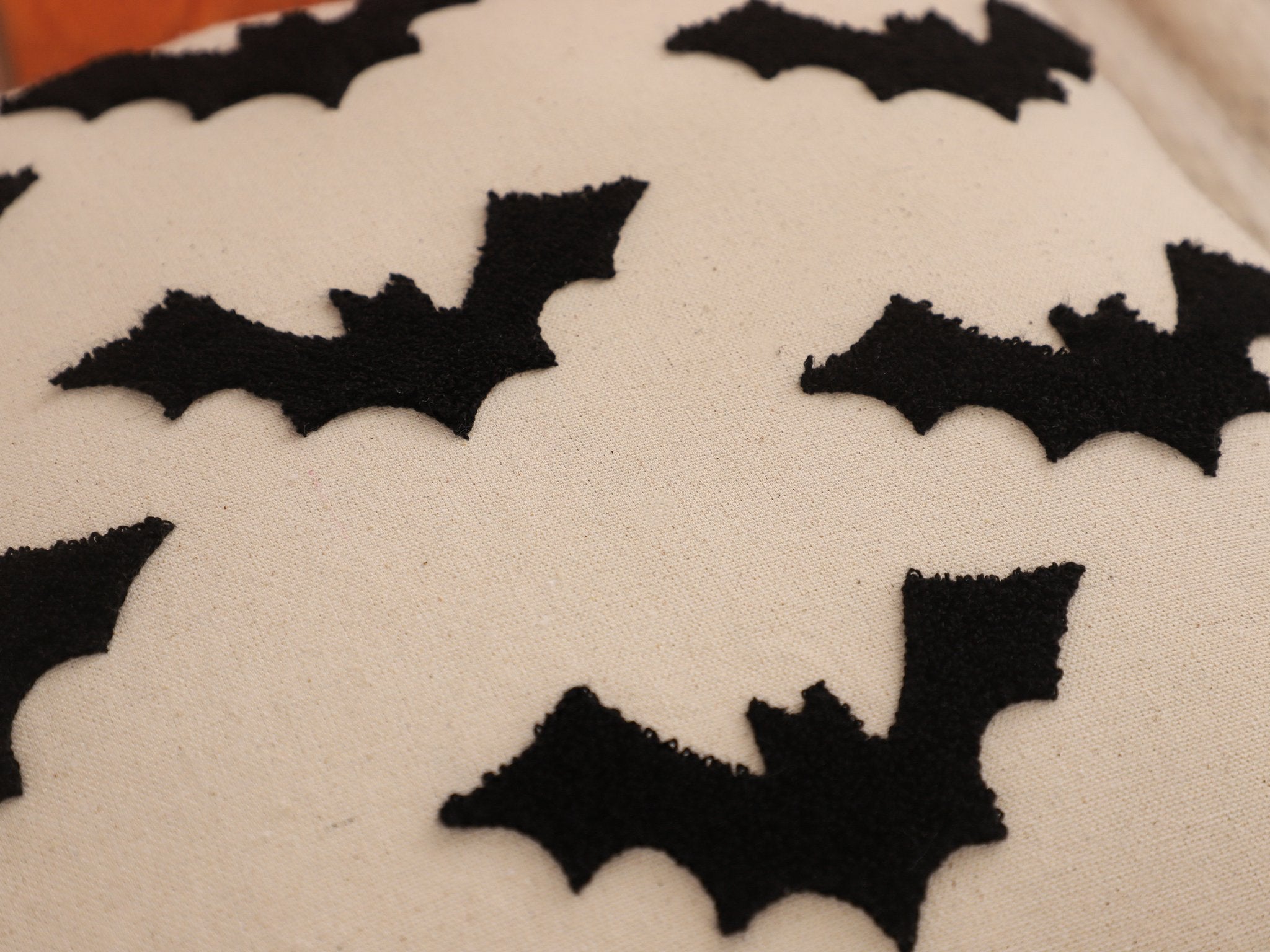Close-up of a cream-colored pillow cover with black embroidered bats scattered across the surface.