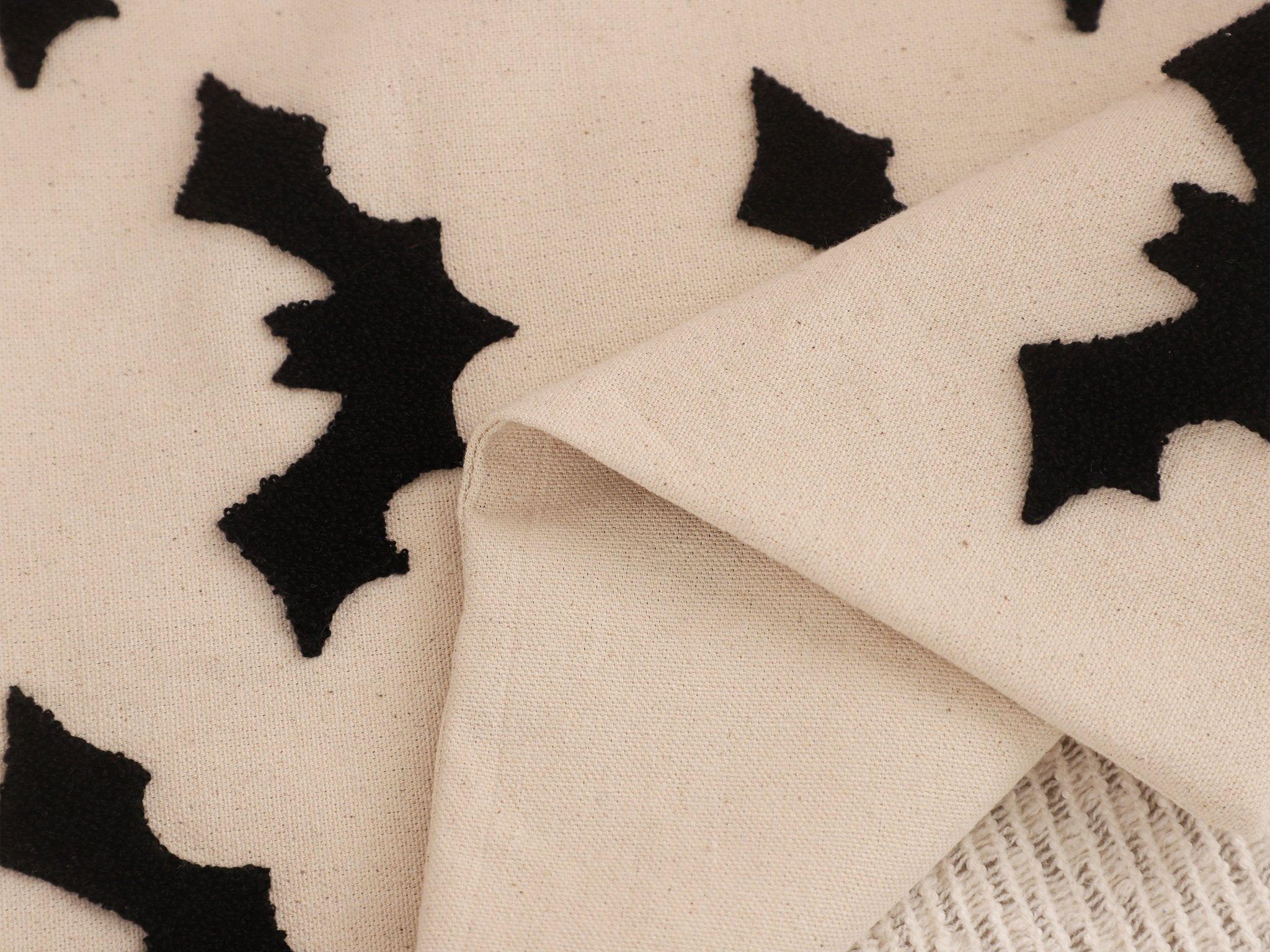 Close-up of a beige fabric with black embroidered bat shapes, folded to show texture.