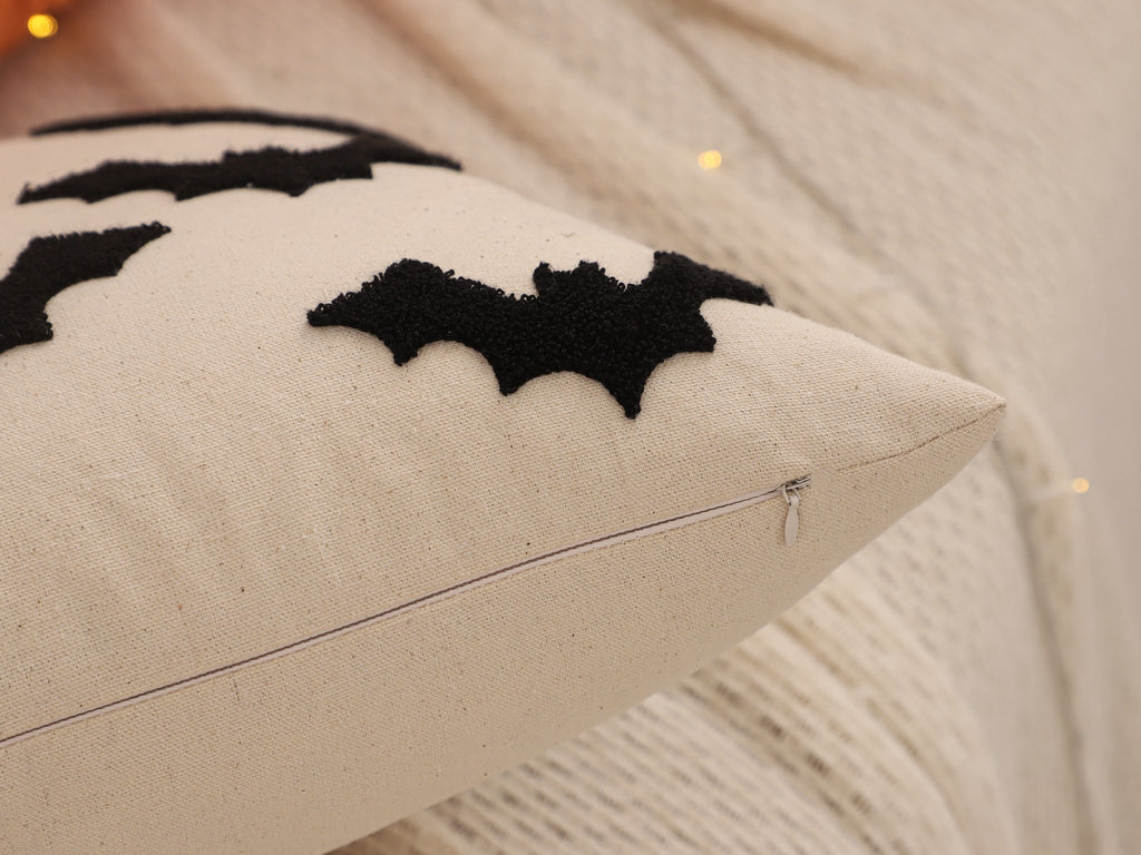 Close-up of a cream-colored Halloween pillow cover with black embroidered bats and a visible zipper.