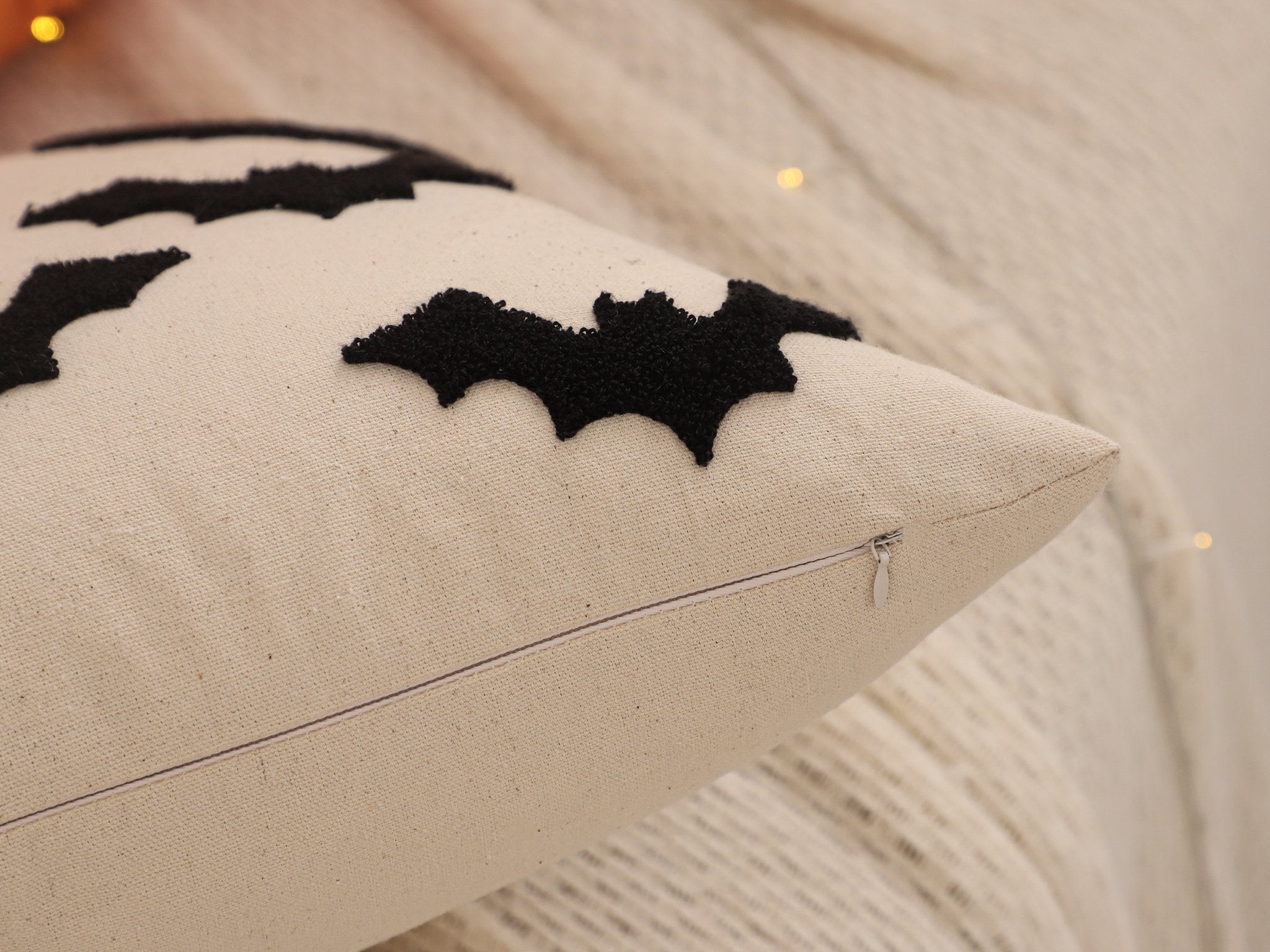 Close-up of a cream-colored Halloween pillow cover with black embroidered bats and a visible zipper.