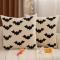 Two cream-colored cotton pillow covers with black embroidered bats, displayed on a sofa with a white knit throw and autumn leaves.