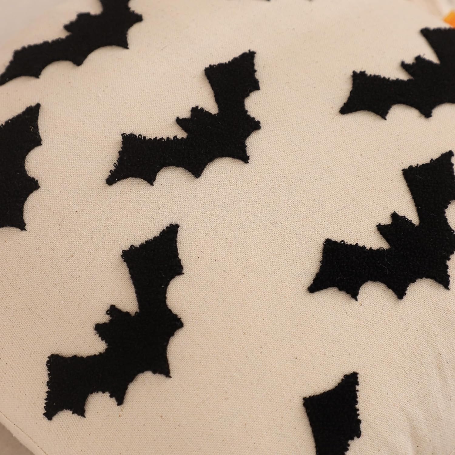 Close-up of a cream-colored pillow cover with black embroidered bat shapes.