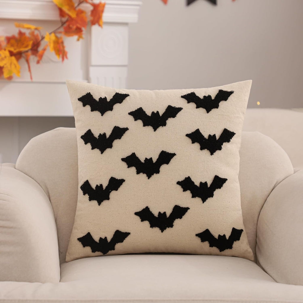 Cream Halloween pillow cover with black embroidered bats, displayed on a sofa with autumn leaves in the background.
