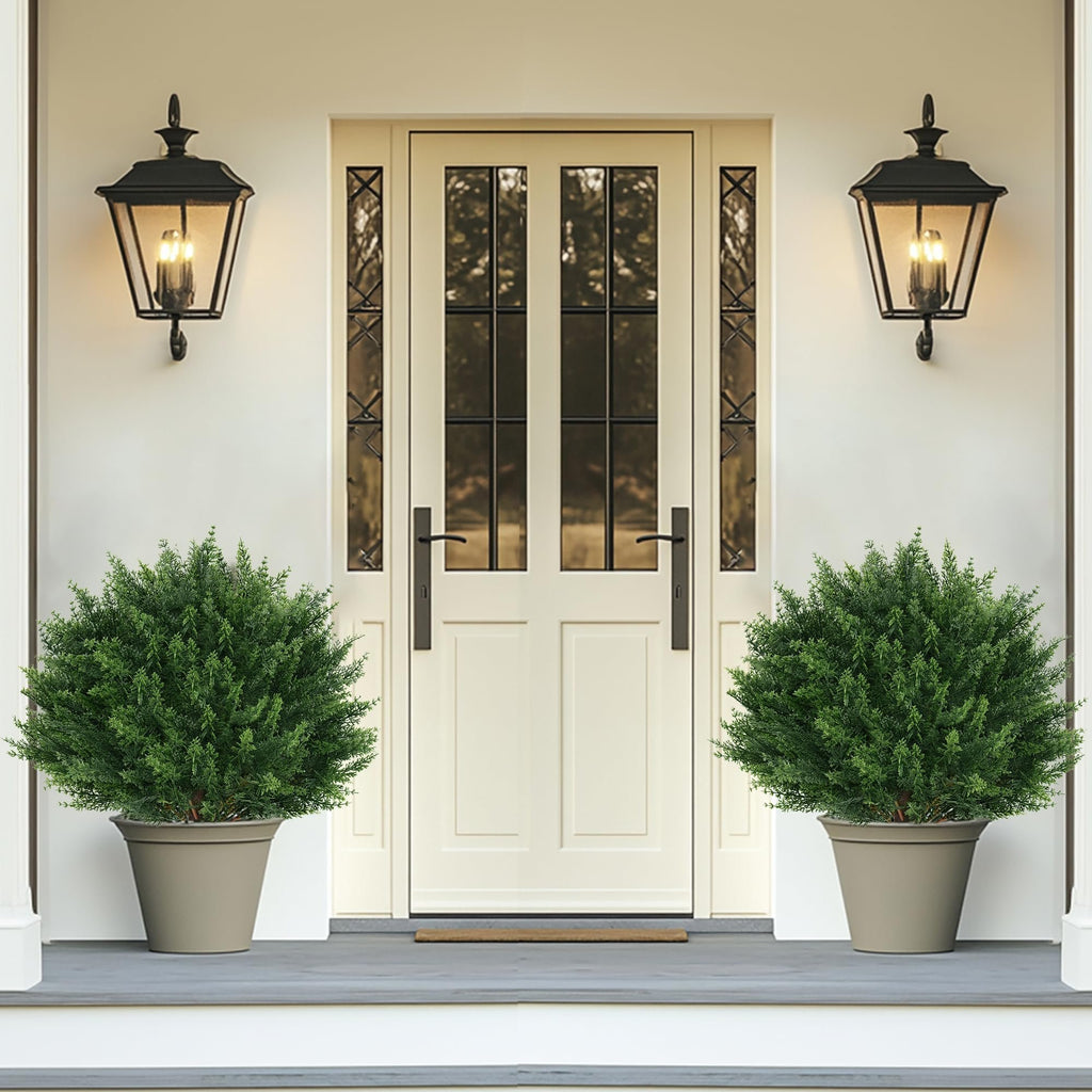Two artificial cypress topiary trees in planters flanking a cream-colored double door on a porch.