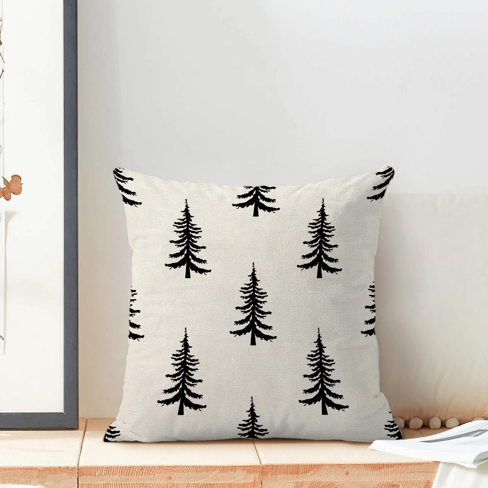 Cream and black Christmas tree pattern pillow cover on a wooden surface with a framed picture.