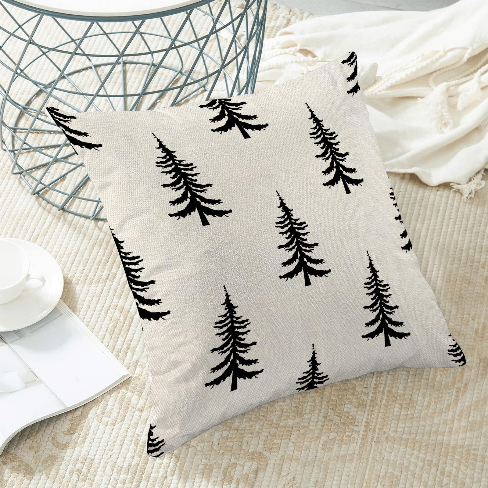 Cream and black Christmas tree pattern pillow cover on a rug with a white cup and magazine.