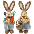 Two straw and sisal Easter bunny figurines, one holding a shovel and carrot, the other holding a basket with an egg.