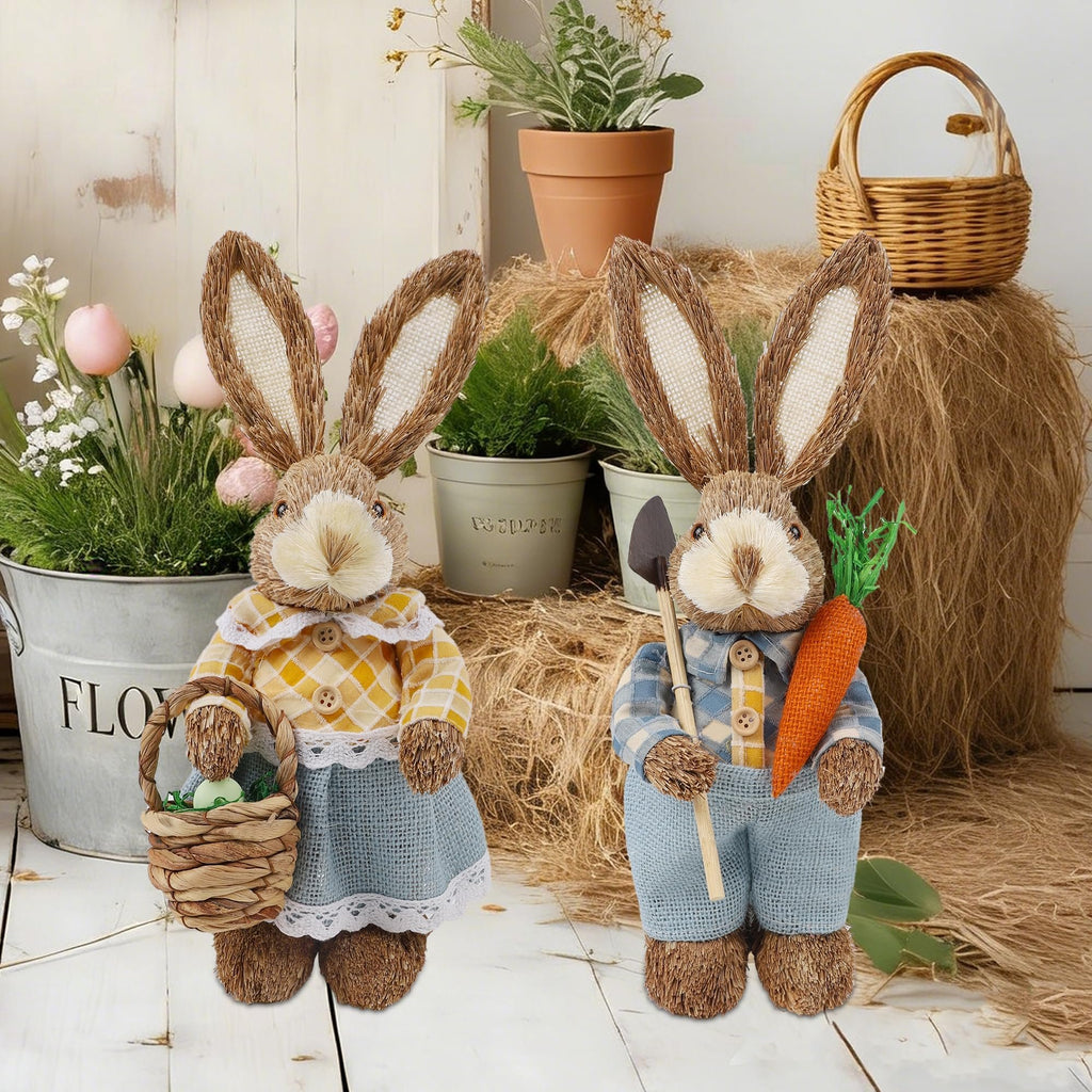 Two rustic Easter bunny figurines, one holding a basket with an egg, the other holding a carrot and shovel, on a hay bale.