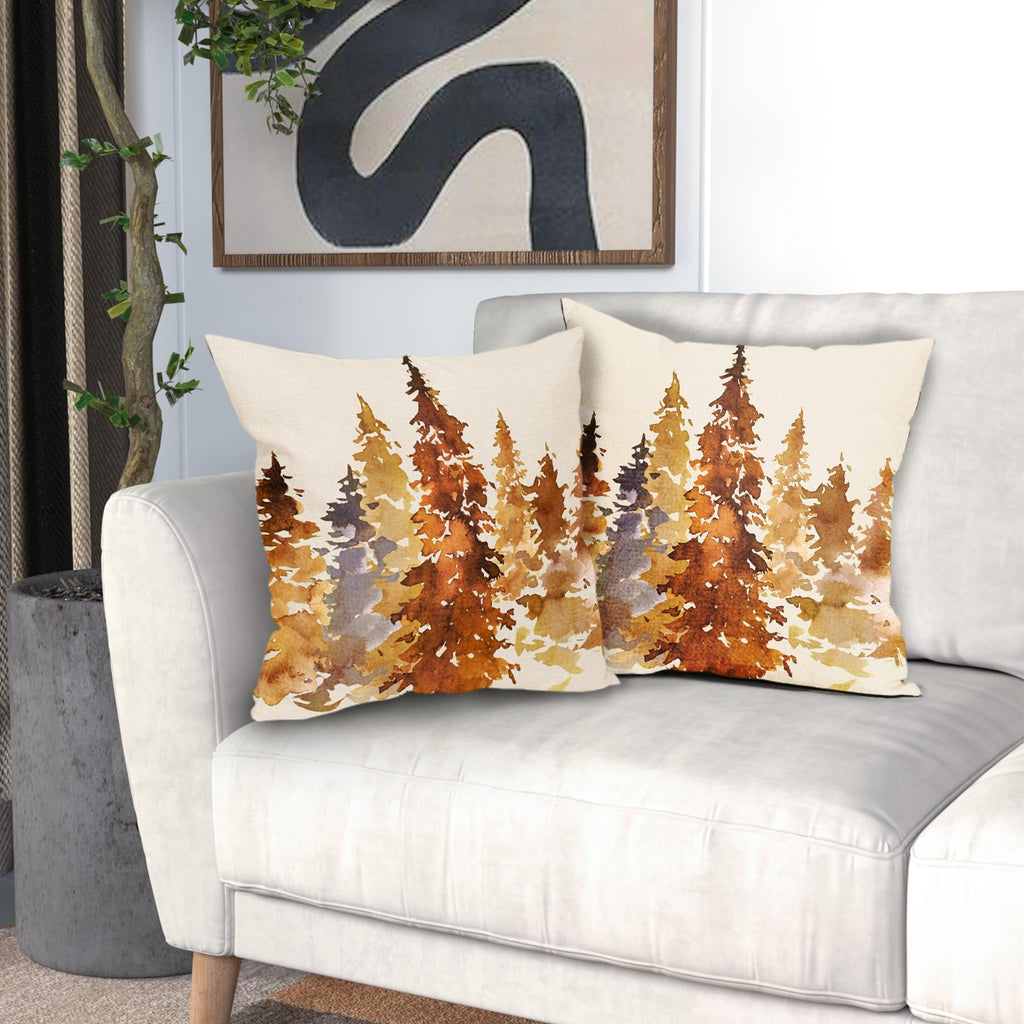 Two square pillow covers with a watercolor forest design in burnt orange and brown hues, displayed on a white sofa.