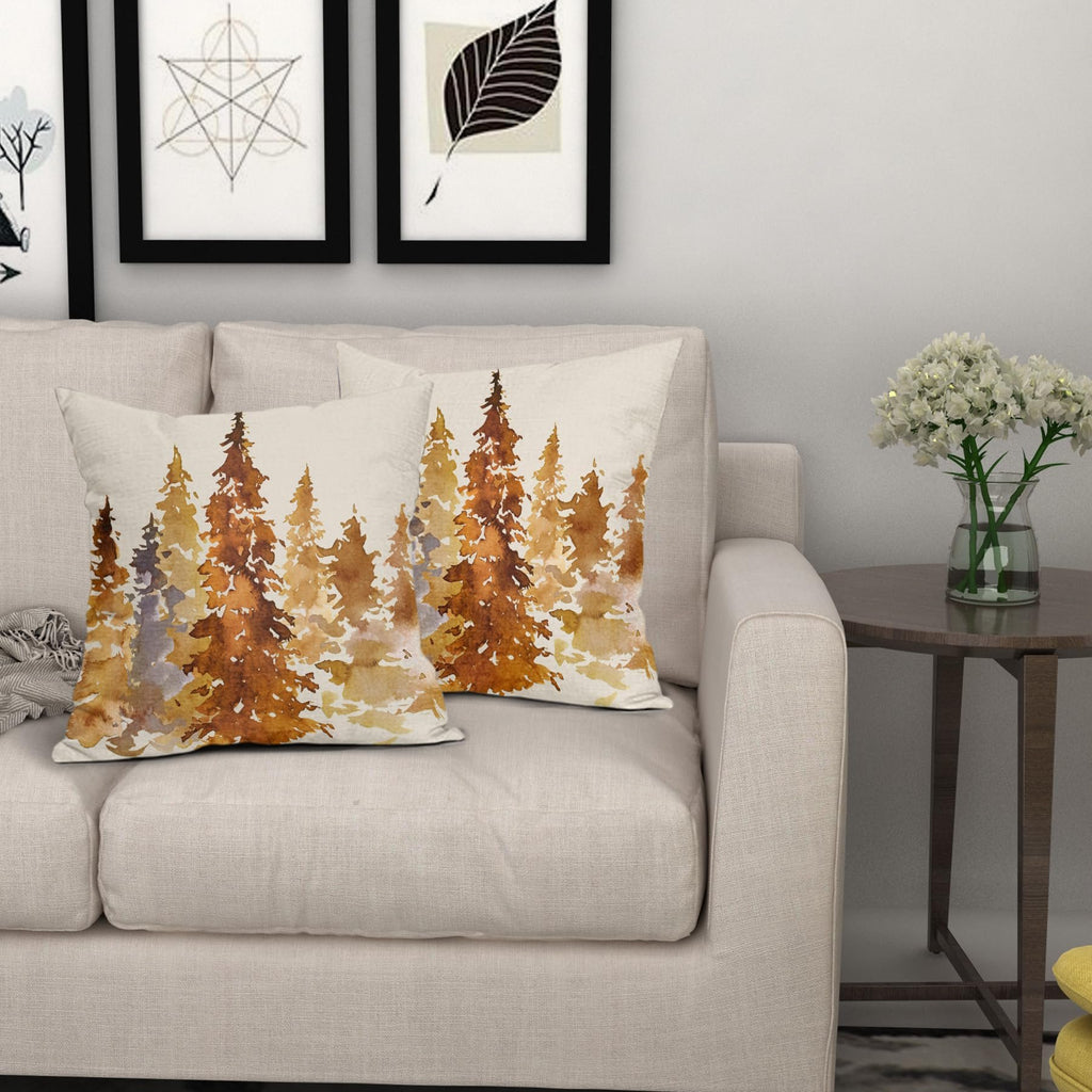 Two square pillow covers with a watercolor forest design in burnt orange and yellow tones, displayed on a sofa.