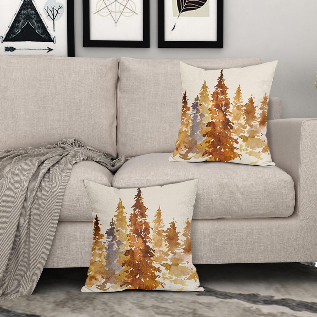 Two square pillow covers with a watercolor forest design in burnt orange and brown hues, displayed on a sofa.