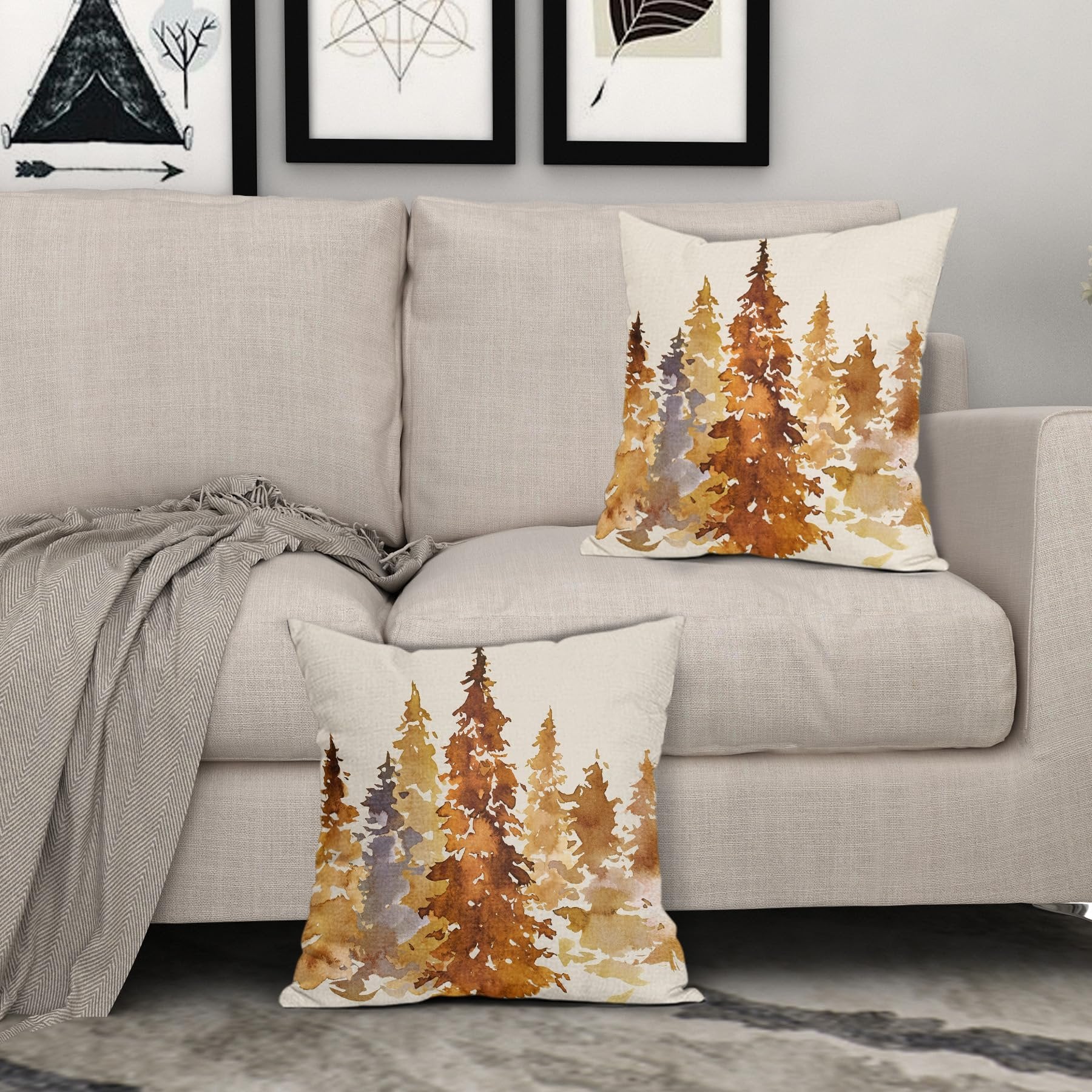 Two square pillow covers with a watercolor forest design in burnt orange and brown hues, displayed on a sofa.