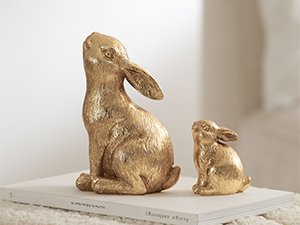Two gold resin bunny figurines, one large and one small, displayed on a book.