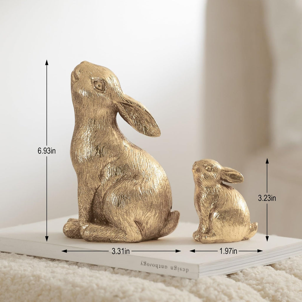 Two gold resin bunny figurines, one large and one small, displayed on a book with dimensions indicated.