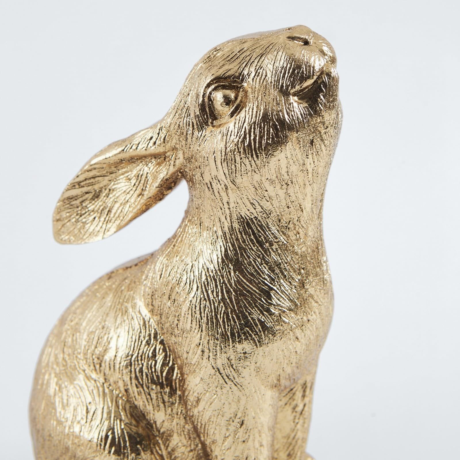 Close-up of a gold resin bunny figurine with textured fur detail, looking upwards against a white background.