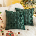 Two green Christmas throw pillow covers with textured tree patterns on a white couch with a Christmas tree in the background.