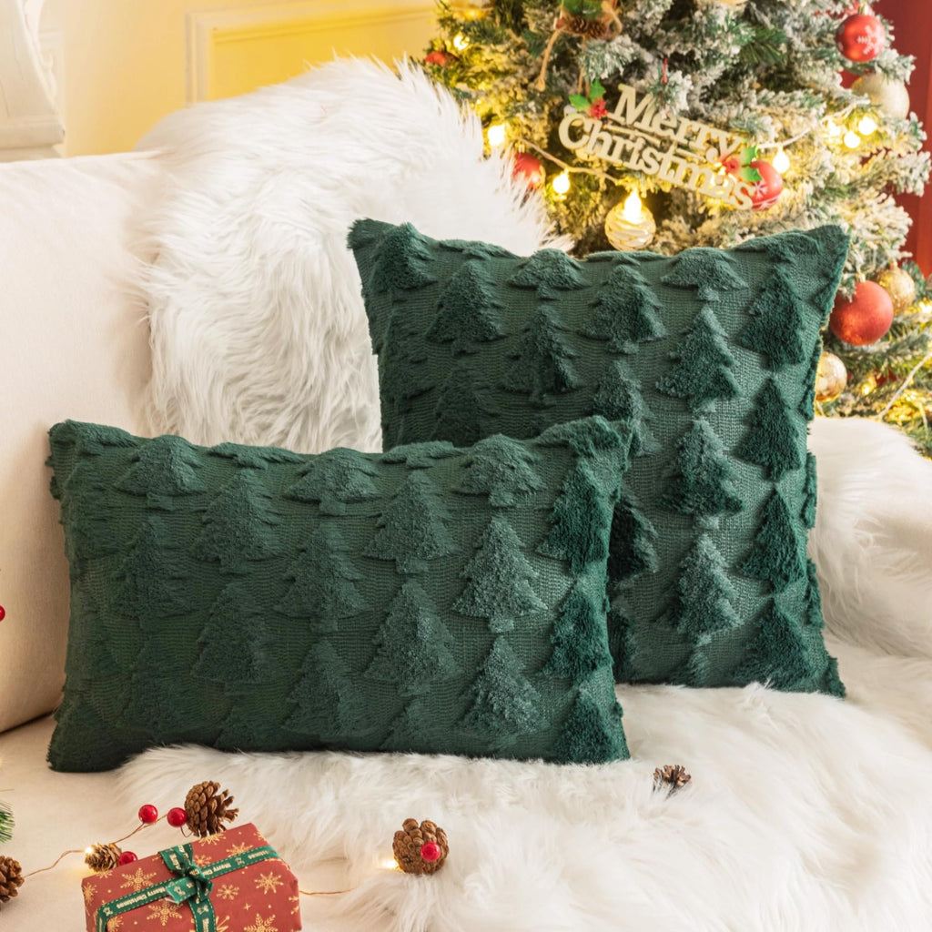 Two green Christmas throw pillow covers with textured tree patterns on a white faux fur rug, with a decorated Christmas tree in the background.
