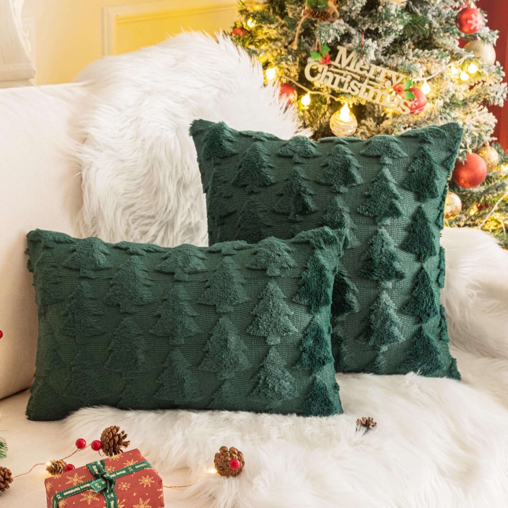Two green Christmas throw pillow covers with textured tree patterns on a white faux fur rug, with a decorated Christmas tree in the background.