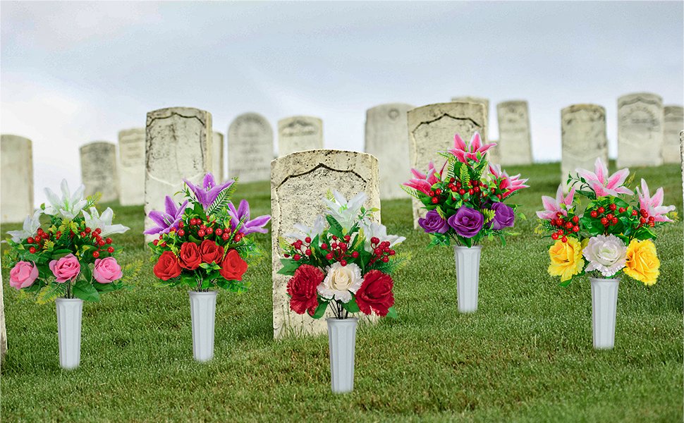 Five artificial flower bouquets in white vases arranged in front of cemetery headstones on a grassy hill.