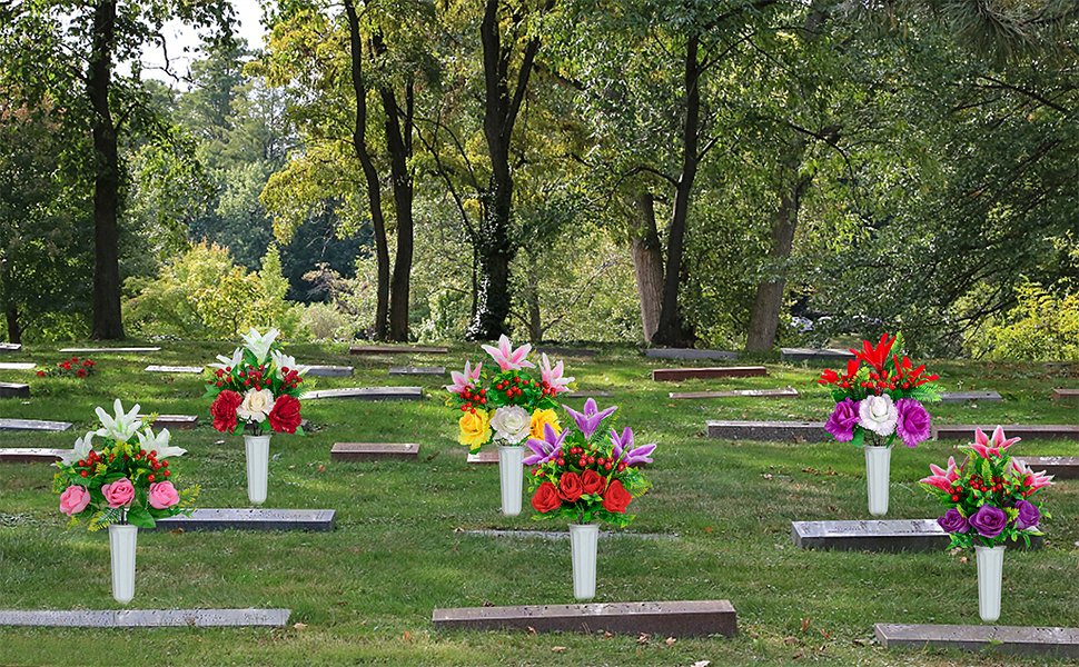 Assortment of artificial cemetery flower bouquets in white vases placed on gravesites, featuring lilies, roses, and red berries.