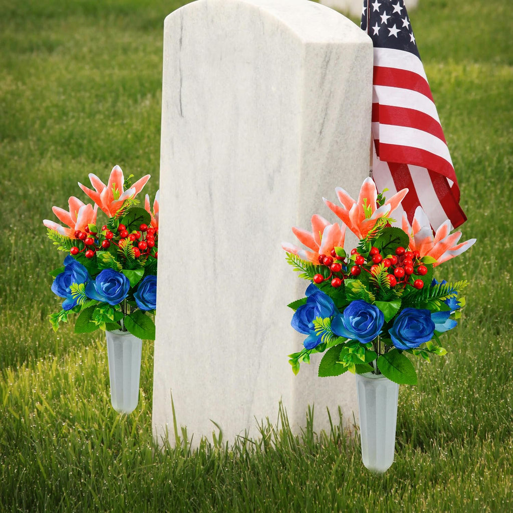 Two artificial flower bouquets with lilies, roses, and berries in plastic vases placed at the base of a tombstone with an American flag.