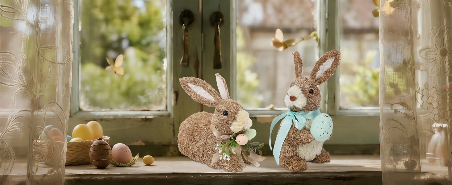 Two sisal bunny figurines with Easter eggs and ribbons on a windowsill, with sheer curtains and a blurred outdoor background.