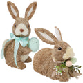 Two sisal bunny figurines, one holding an egg and wearing a blue ribbon, the other adorned with eggs and greenery.