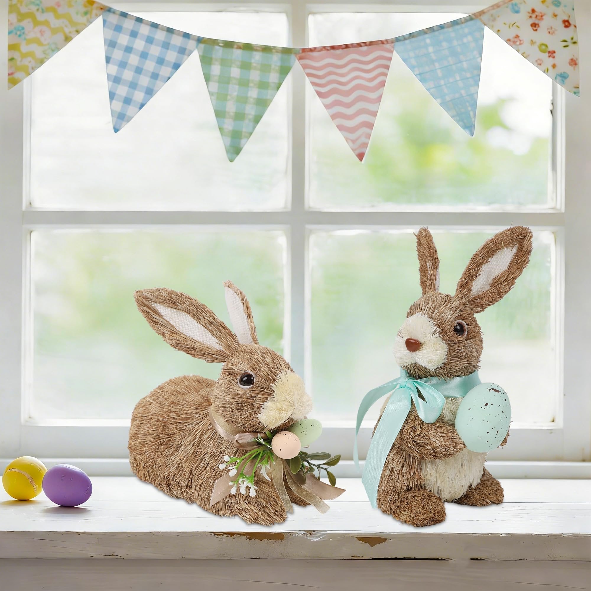 Two sisal bunny figurines with Easter eggs and decorative ribbons, displayed on a windowsill with a festive banner overhead.