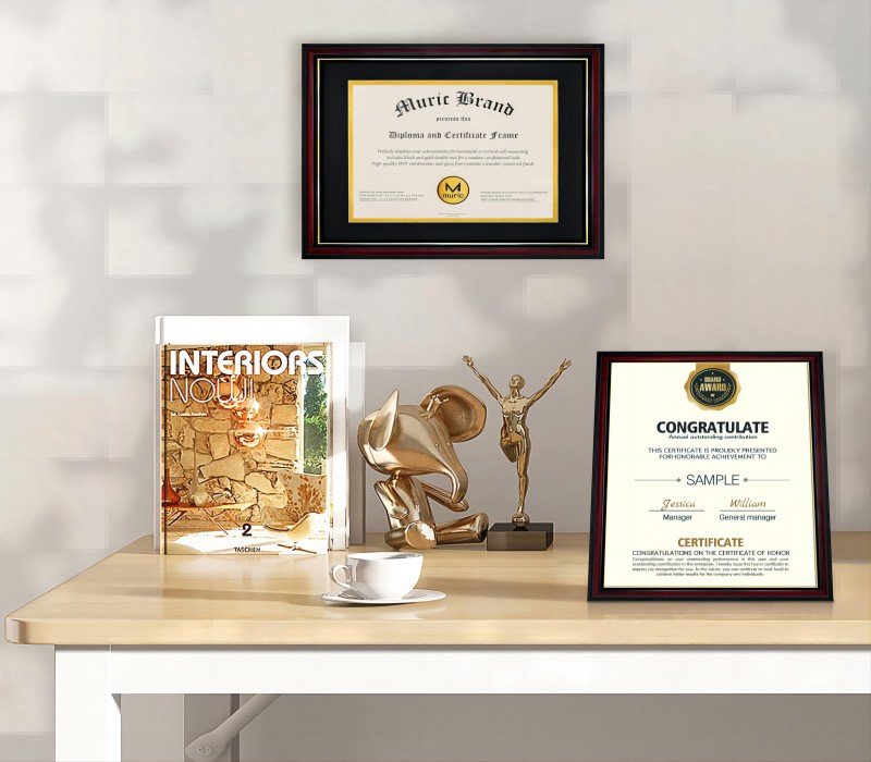 Two diploma frames on a desk with decorative statues and a book. One frame displays a certificate with "Muric Brand" text.