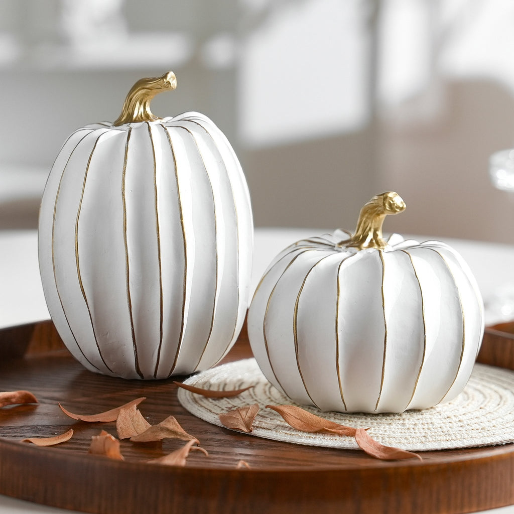 Two white and gold decorative pumpkins on a wooden tray with dried leaves
