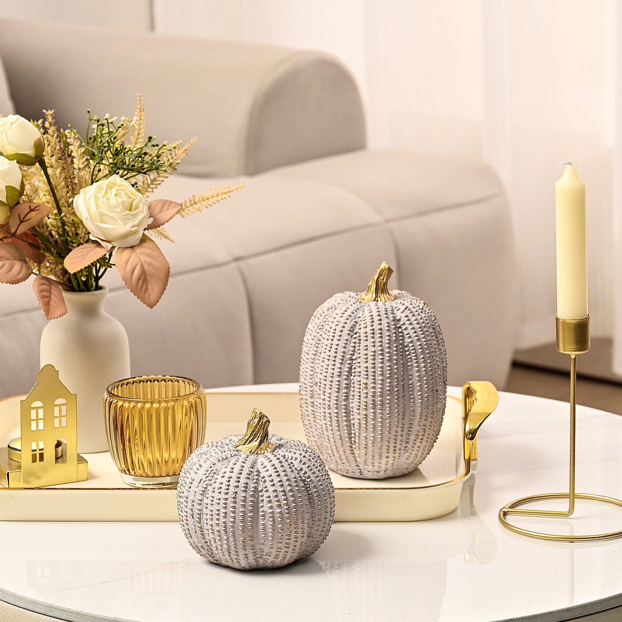 Two decorative white and gold pumpkins on a tray with a vase of flowers and a candle.