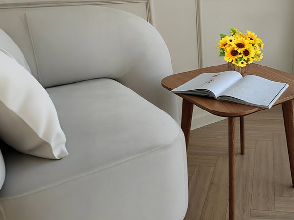 Artificial sunflowers in a pot on a wooden side table next to a sofa with a book open on the table.