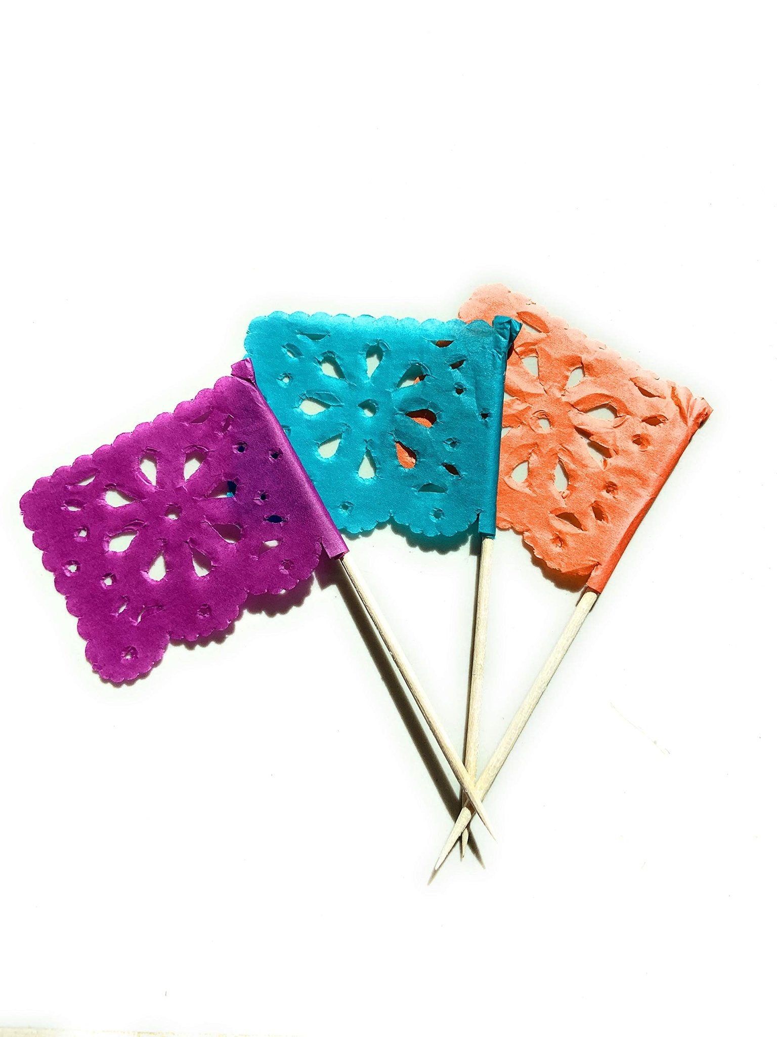 Three mini papel picado flag picks in purple, teal, and orange on wooden sticks against a white background.