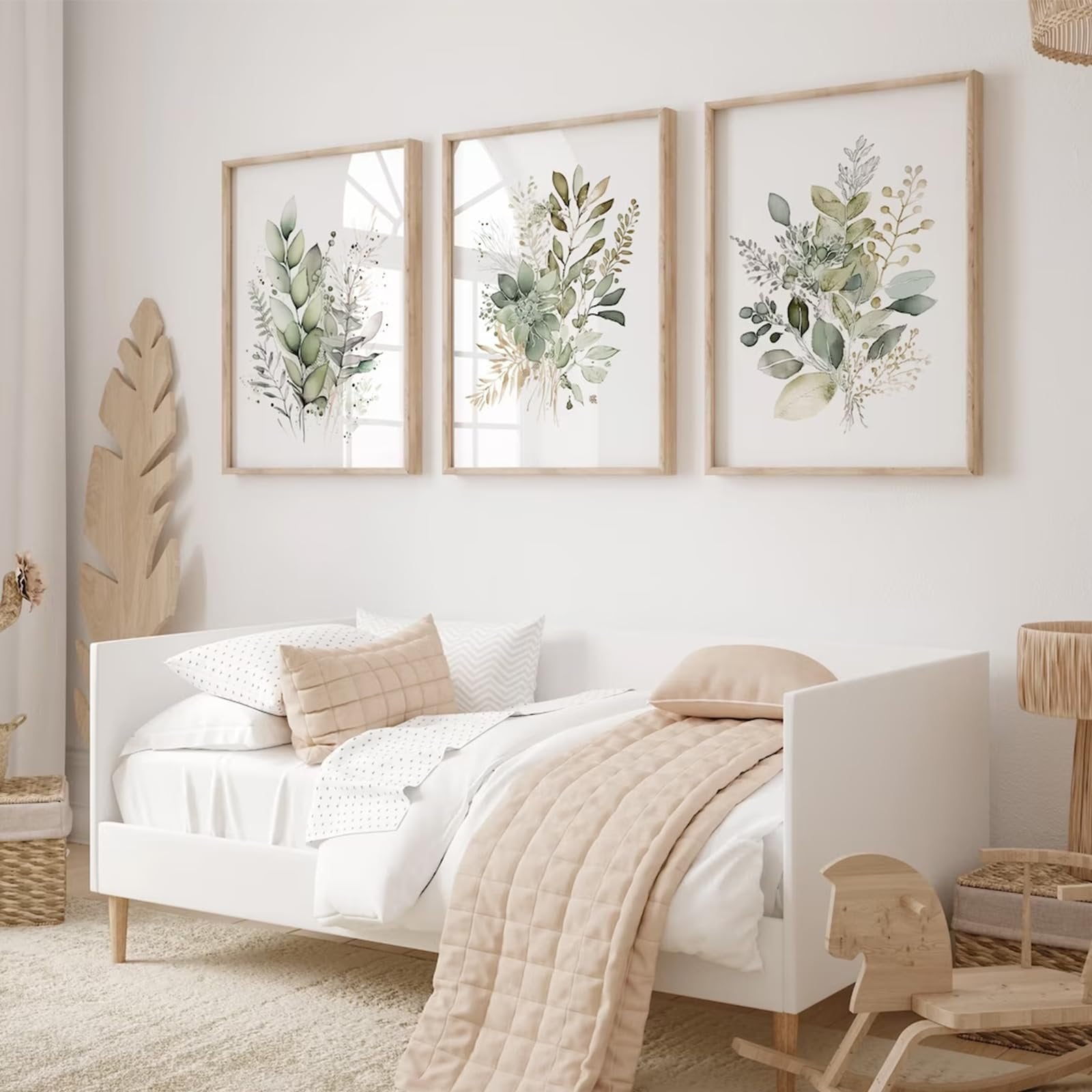 Three unframed watercolor botanical prints with sage green leaves and wildflowers hanging above a white bed.