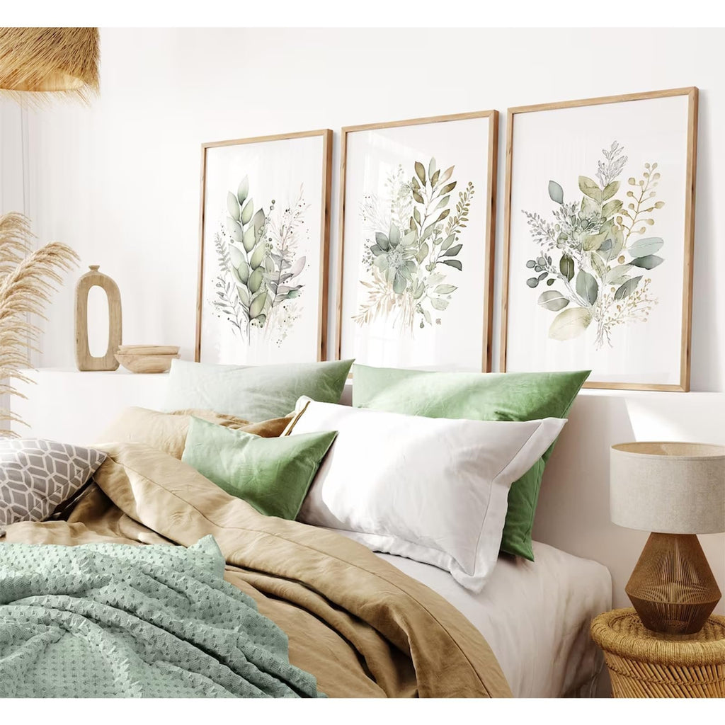 Three unframed watercolor botanical prints with sage green leaves and wildflowers hanging above a bed with green and tan bedding.