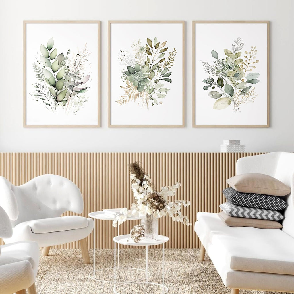 Three framed watercolor botanical prints with sage green leaves and wildflowers displayed on a wall above a slatted wood panel.