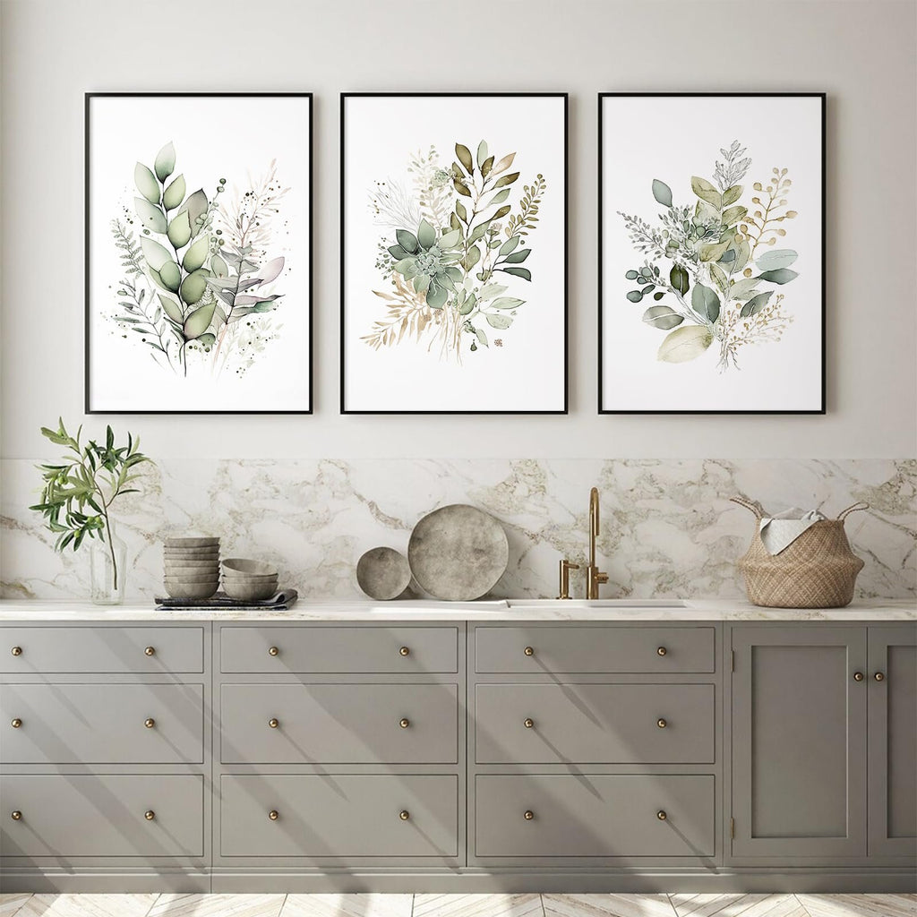 Three framed watercolor botanical prints with sage green leaves and wildflowers displayed above a kitchen counter.