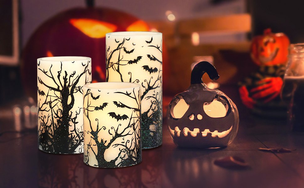 Three flameless LED pillar candles with black bat and tree decals, next to a lit ceramic jack-o'-lantern.