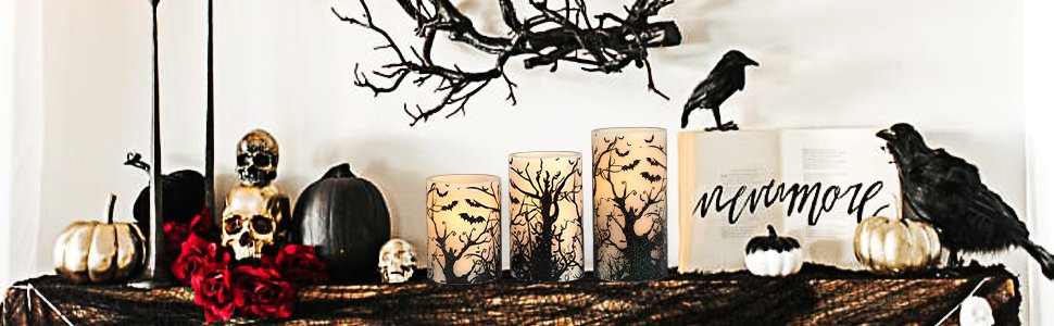 Three flameless LED pillar candles with black bat and tree decals, displayed on a Halloween-themed mantelpiece with skulls and pumpkins.