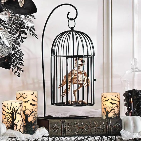 Three flameless LED pillar candles with Halloween tree and bat decals displayed on a shelf with a decorative birdcage containing a skeleton.