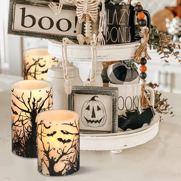 Two flameless LED pillar candles with black bat and tree decals, set on a tiered tray with Halloween decor.