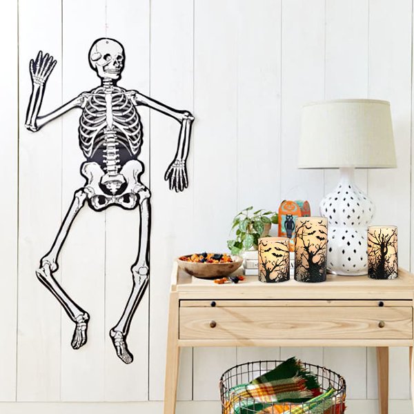 Flameless LED pillar candles with black bat and tree designs on a table with a skeleton decoration