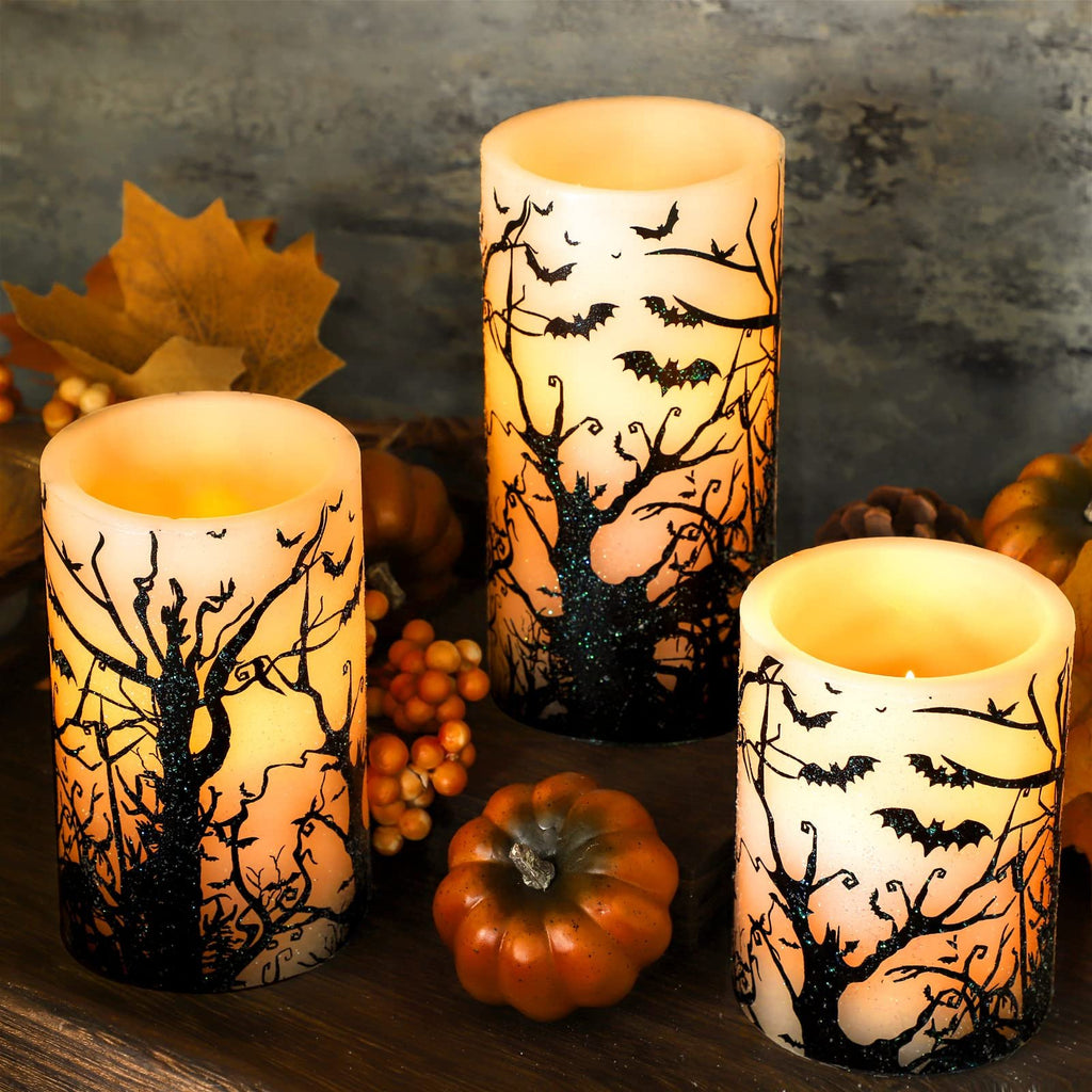 Three flameless LED pillar candles with black bat and tree decals, set on a wooden surface with autumn decorations.